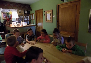 Dzieci siedzą przy prostokątnym stole i jedzą ciasteczka.